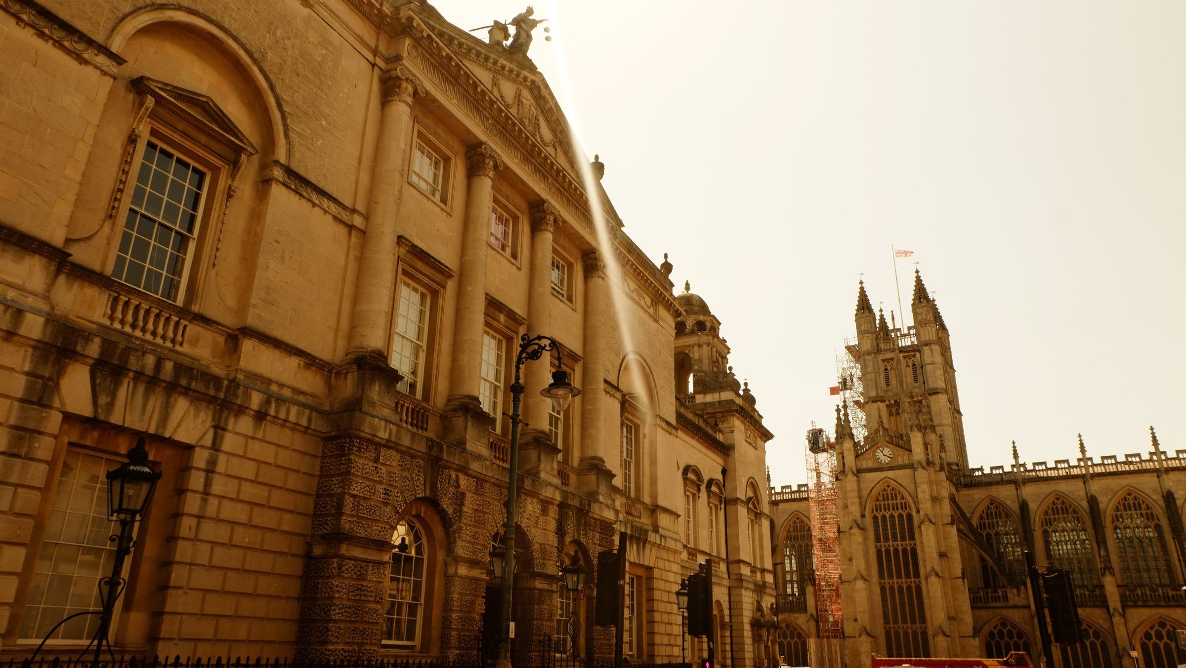 The columned stone front of the Guildhall with an iron street lamp, Bath Abbey rising beyond it