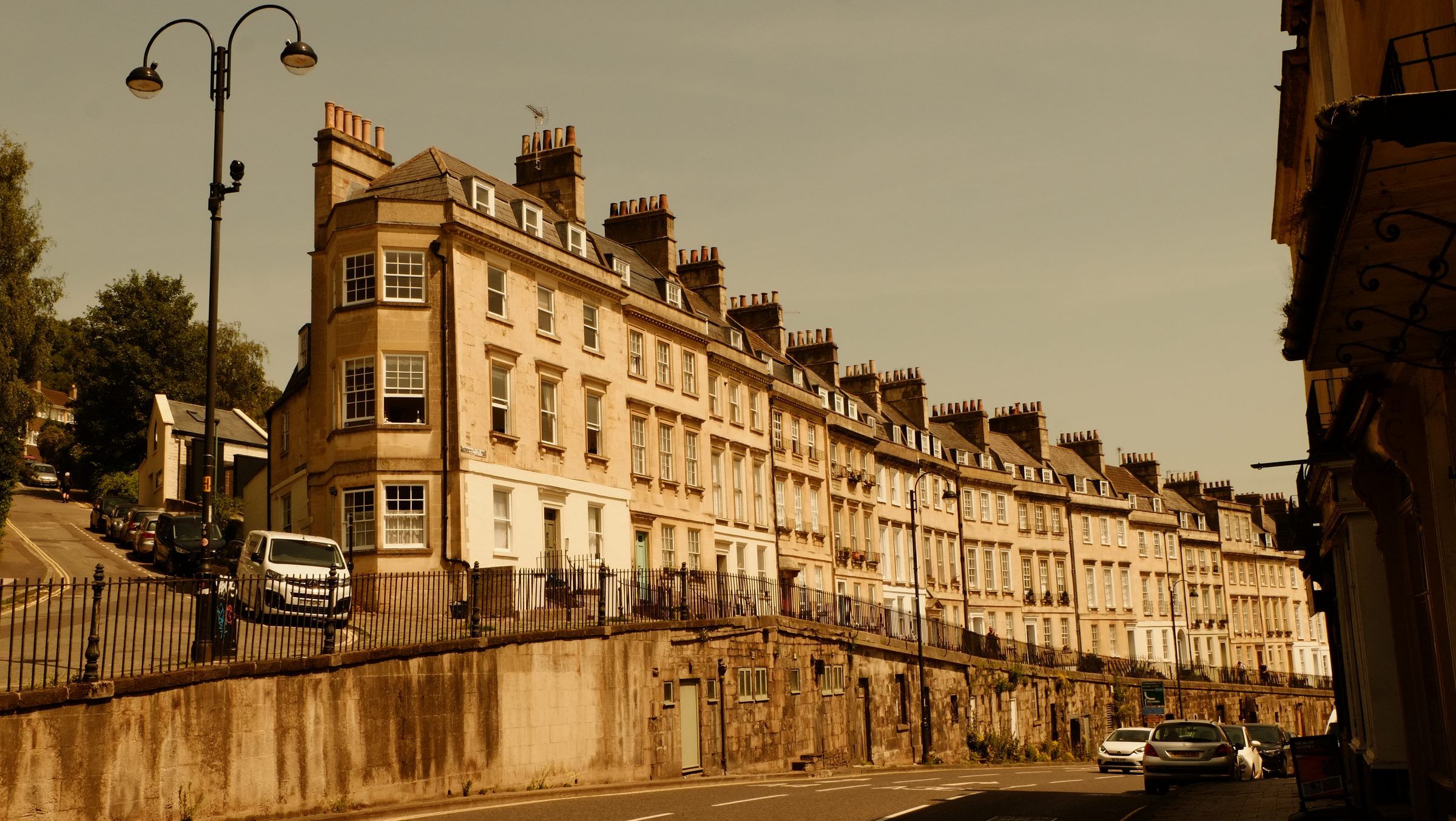 A long terrace of Georgian townhouses with tall chimneys climbing a hill above a raised stone pavement