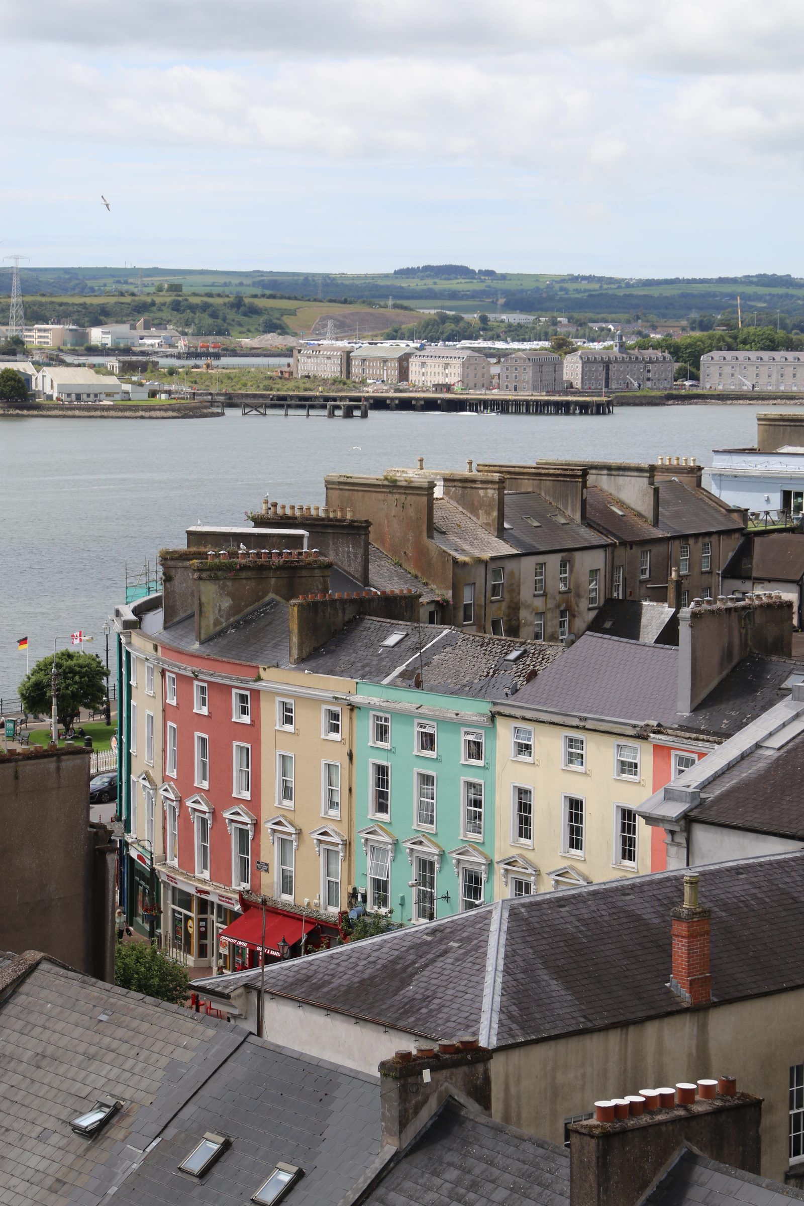 A terrace of pastel-painted houses on the waterfront seen over slate rooftops, the harbour and docks beyond
