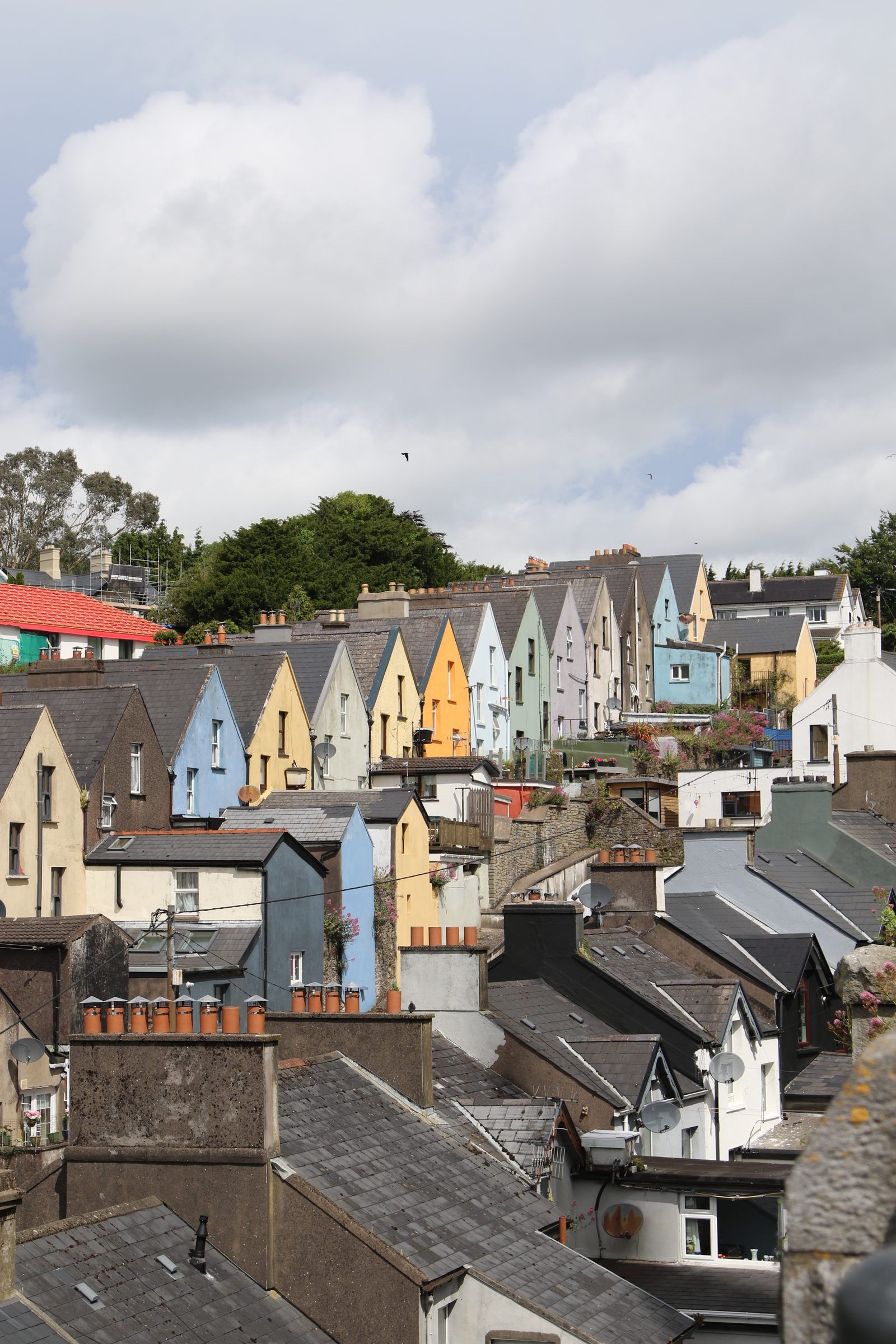 A steep row of gabled houses in pastel blues, yellows and greens stepping up a hill above grey rooftops and chimneys