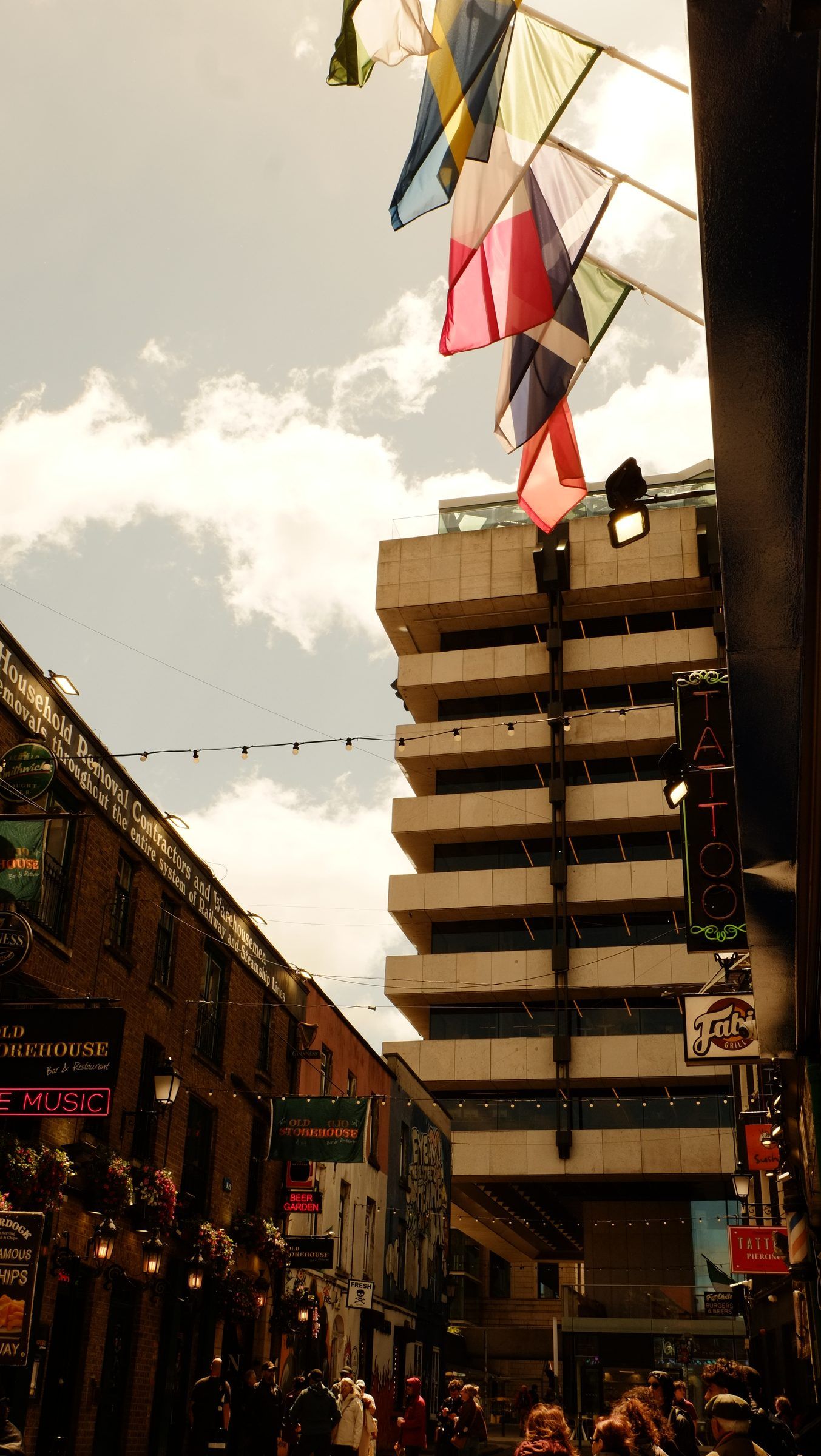 A row of flags hanging over a busy pub-lined street, a concrete tower block behind
