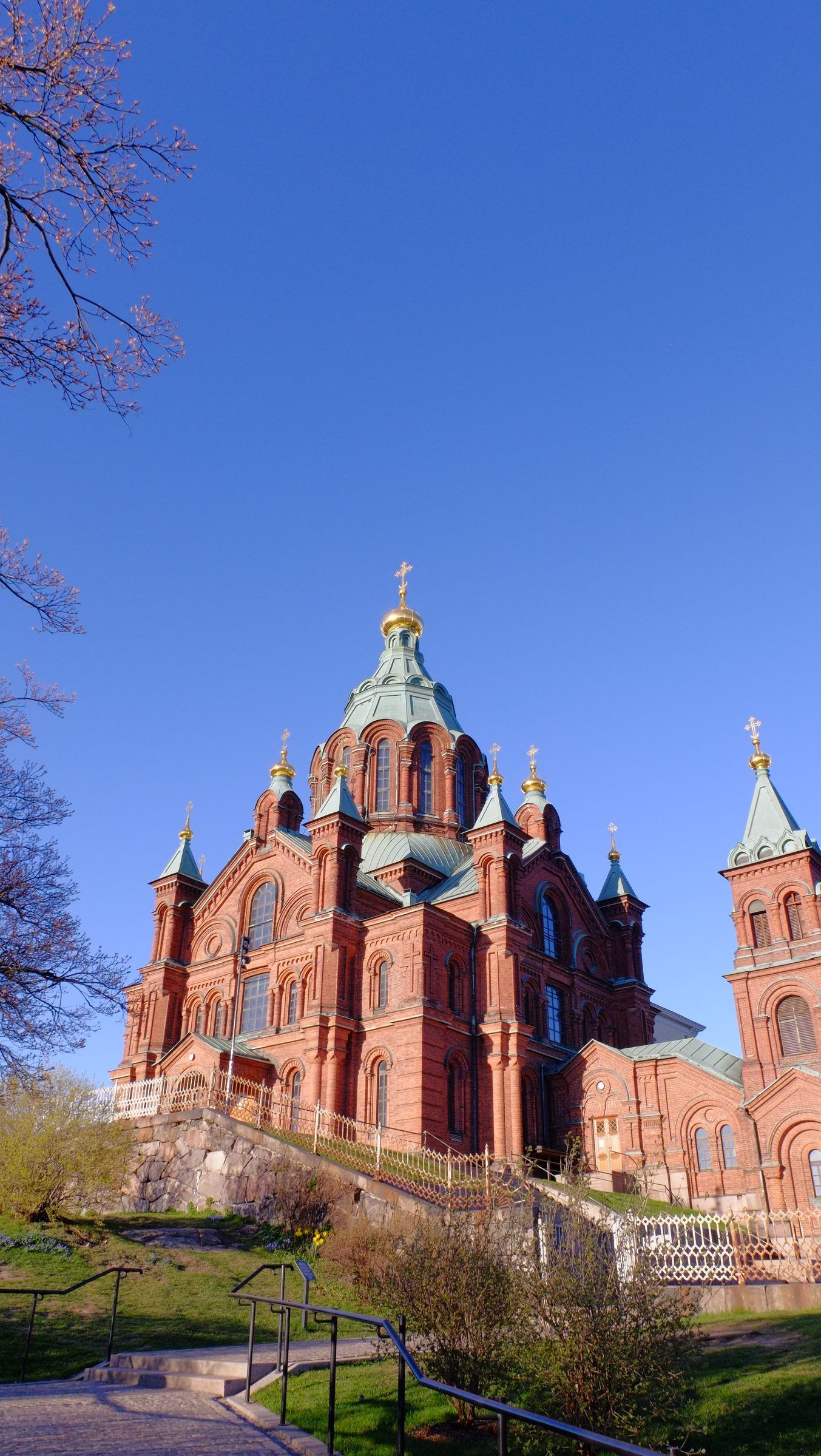 The red-brick Uspenski Cathedral with green roofs and gold onion domes on a hill against a deep blue sky