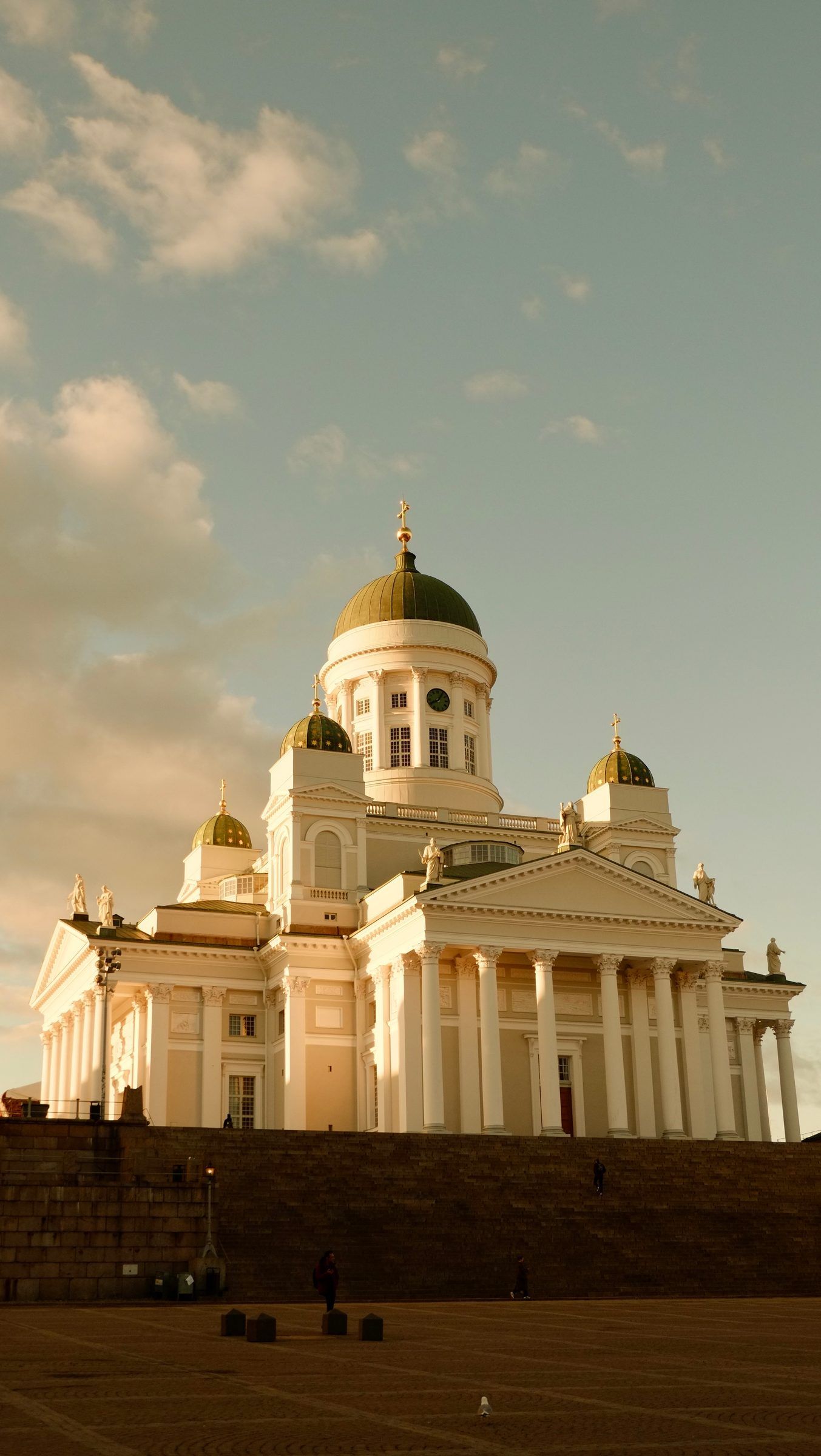 The white cathedral with green domes glowing in warm evening light above the dark steps of the square