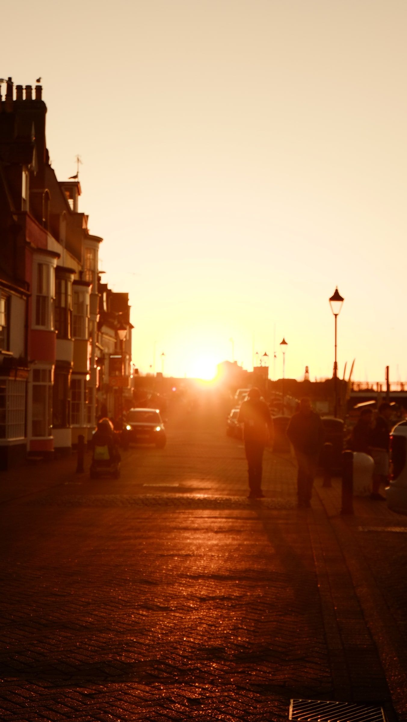 People walking along the seafront promenade towards a setting sun between tall terraced houses